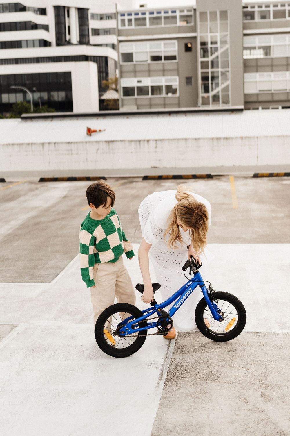A series of four images showing a blue balance bike being ridden on a concrete surface outdoors.
