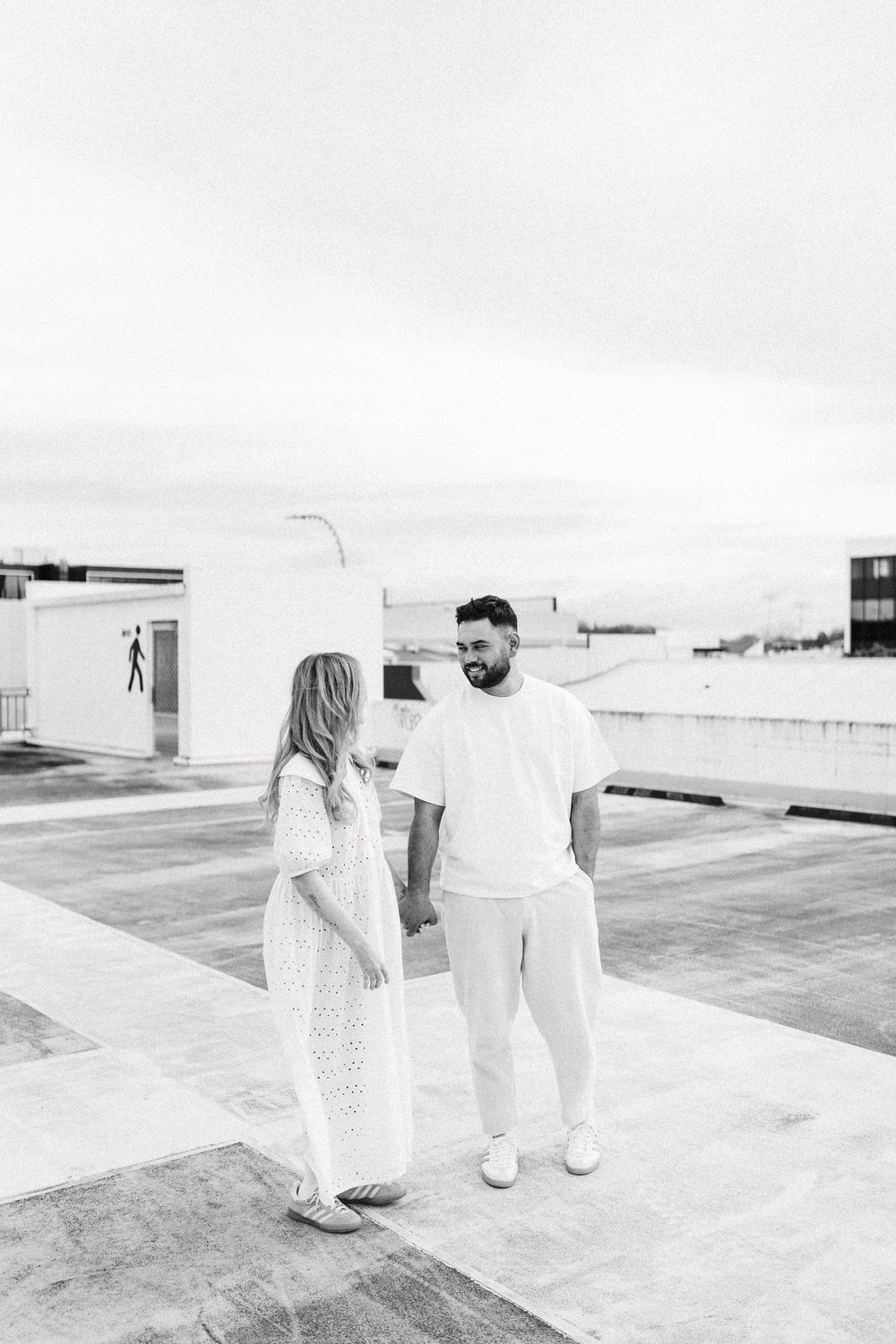 A minimalist black and white sequence of four images showing two people walking on a bright rooftop or terrace space.