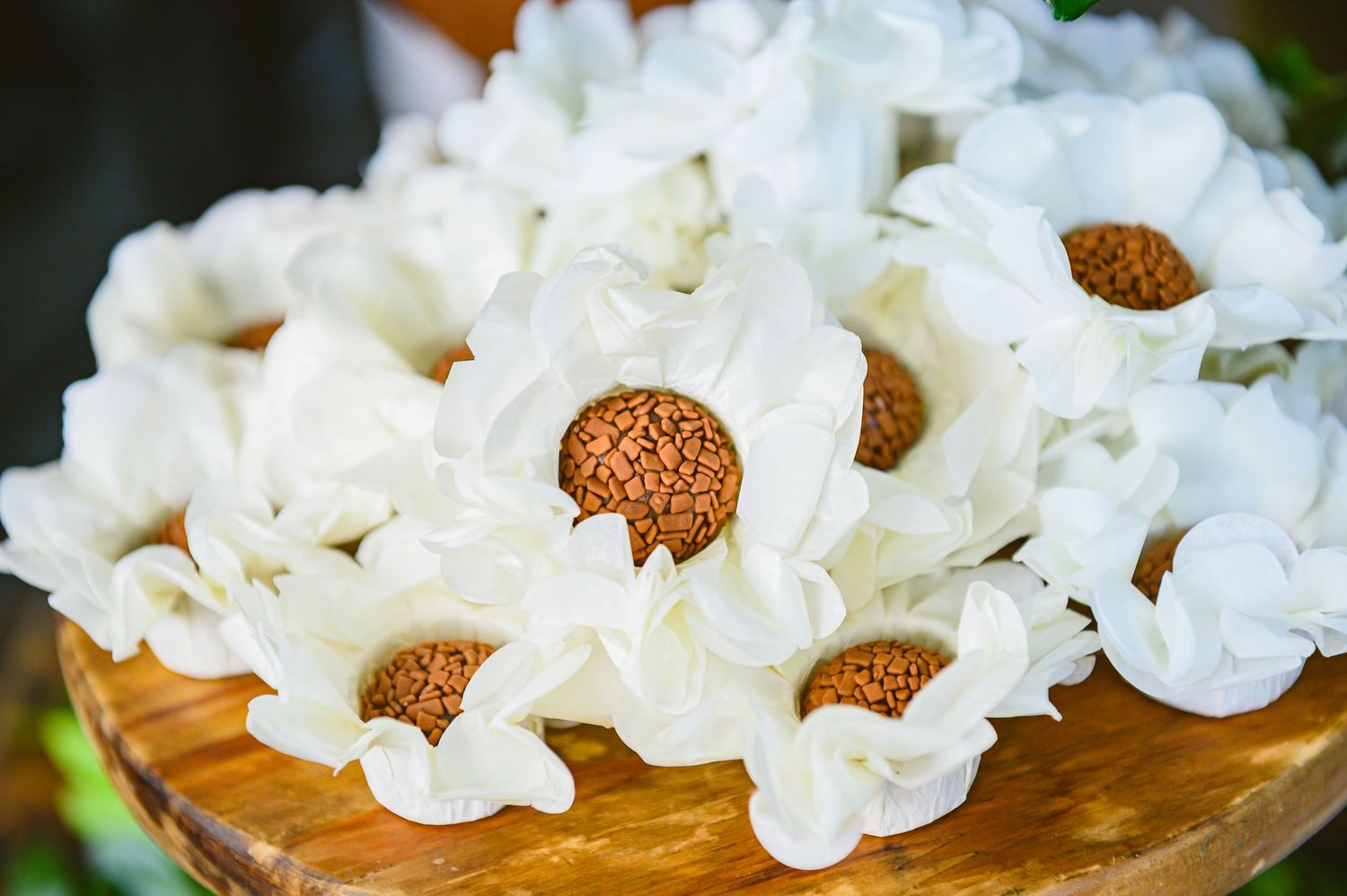 Fresh white ruffle-petaled carnations with brown centers arranged in a rustic wooden bowl against green background.
