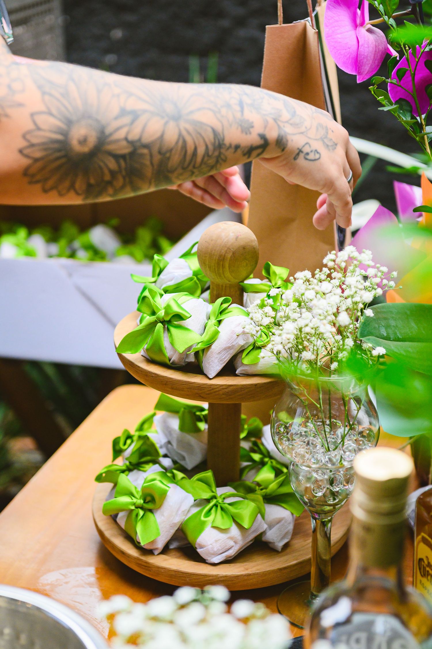 Tattooed arm arranges food and flowers on a wooden two-tiered serving platter with baby's breath in a crystal vase.