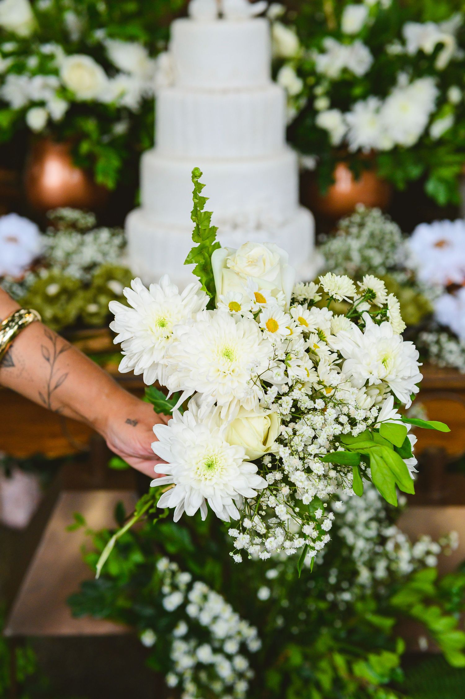 A white wedding cake surrounded by delicate floral arrangements featuring chrysanthemums and baby's breath on a wooden table.
