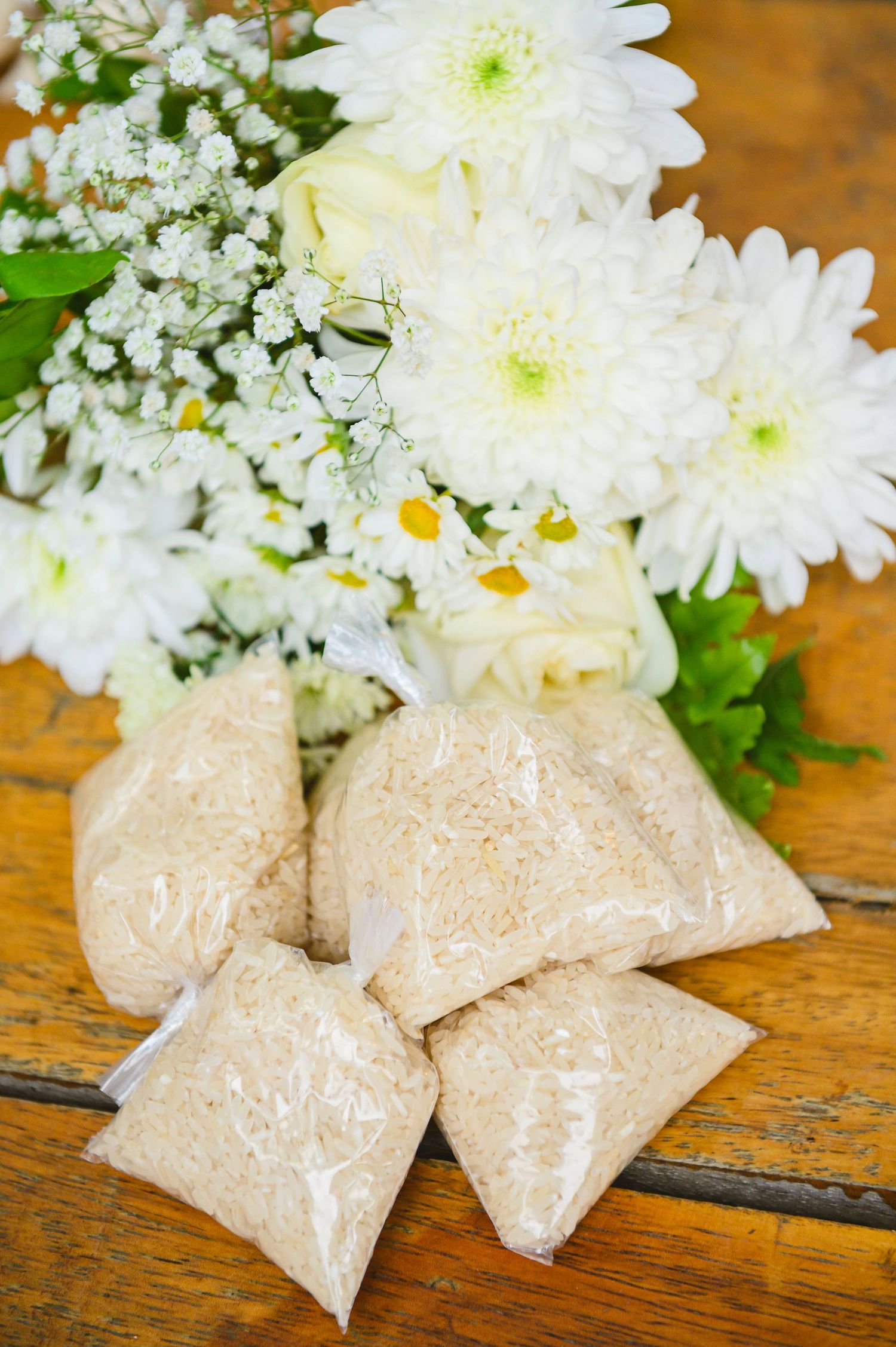 White chrysanthemums and babys breath flowers arranged with small beige sachets on a rustic wooden surface.