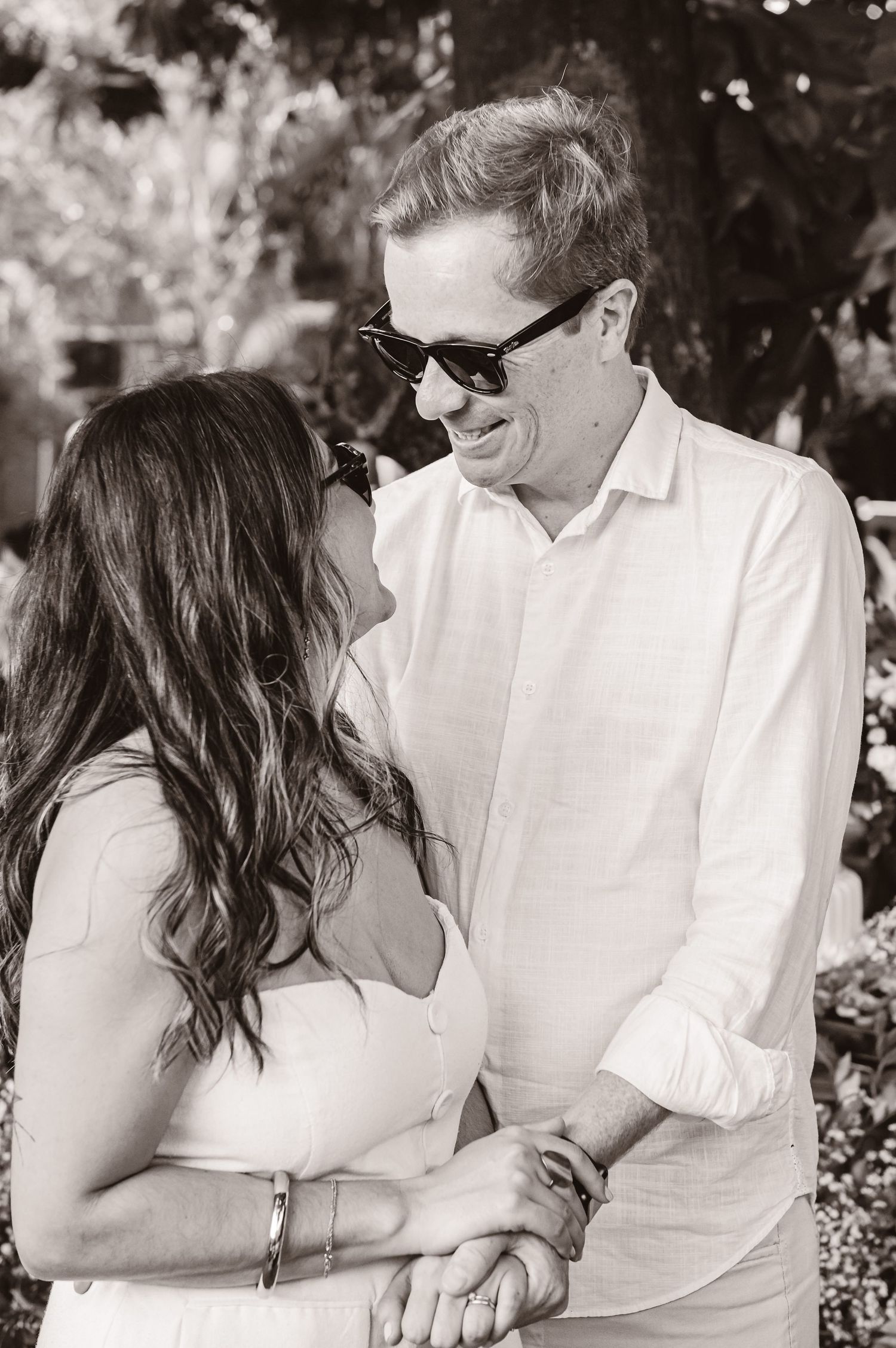 A romantic black and white photo of a couple holding hands and sharing an intimate moment in an outdoor garden setting.