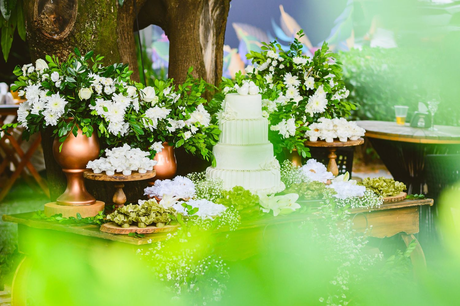 Elegant wedding dessert table with white cake, cupcakes and floral decorations in a dreamy garden setting.