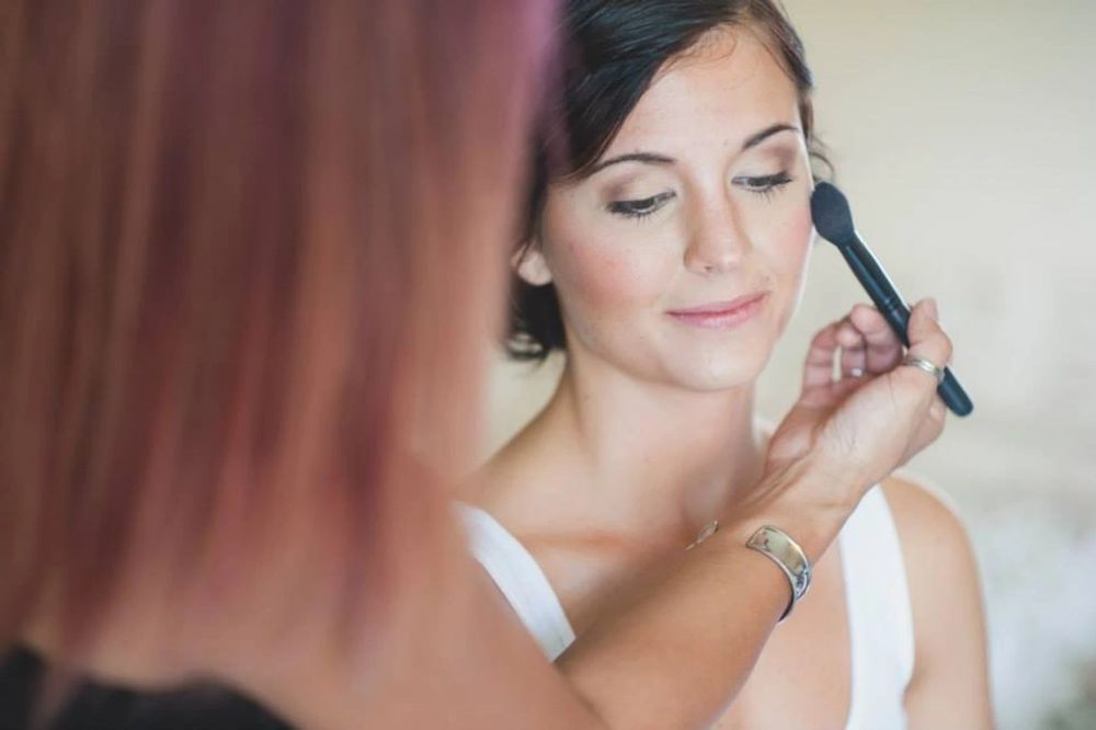 A professional makeup artist applies finishing touches to a bride's eye makeup during wedding preparation.