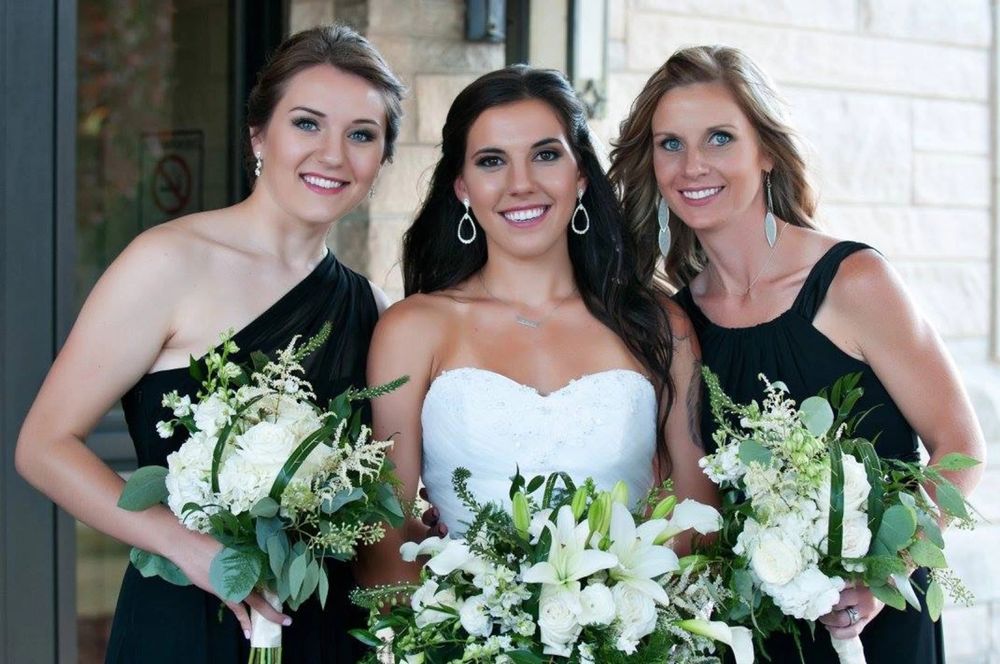Wedding party members holding white floral bouquets pose together while wearing emerald green and white dresses.