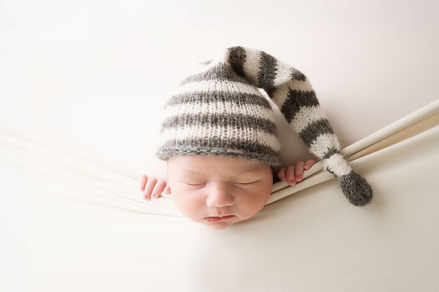 Sleeping baby wearing striped knit hat photographed on white background in studio setting.