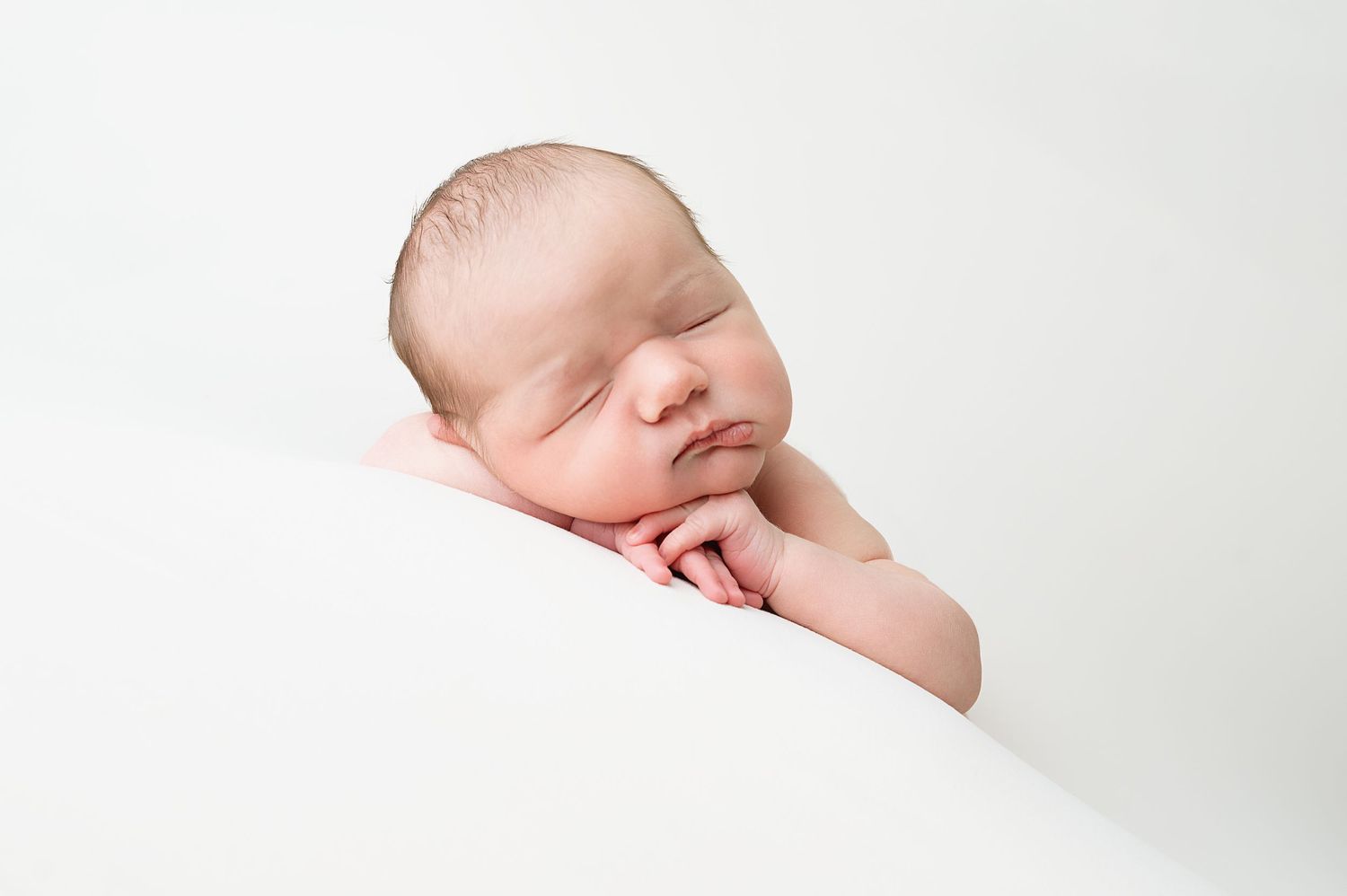 Peaceful newborn sleeping on simple white backdrop in artistic studio pose.