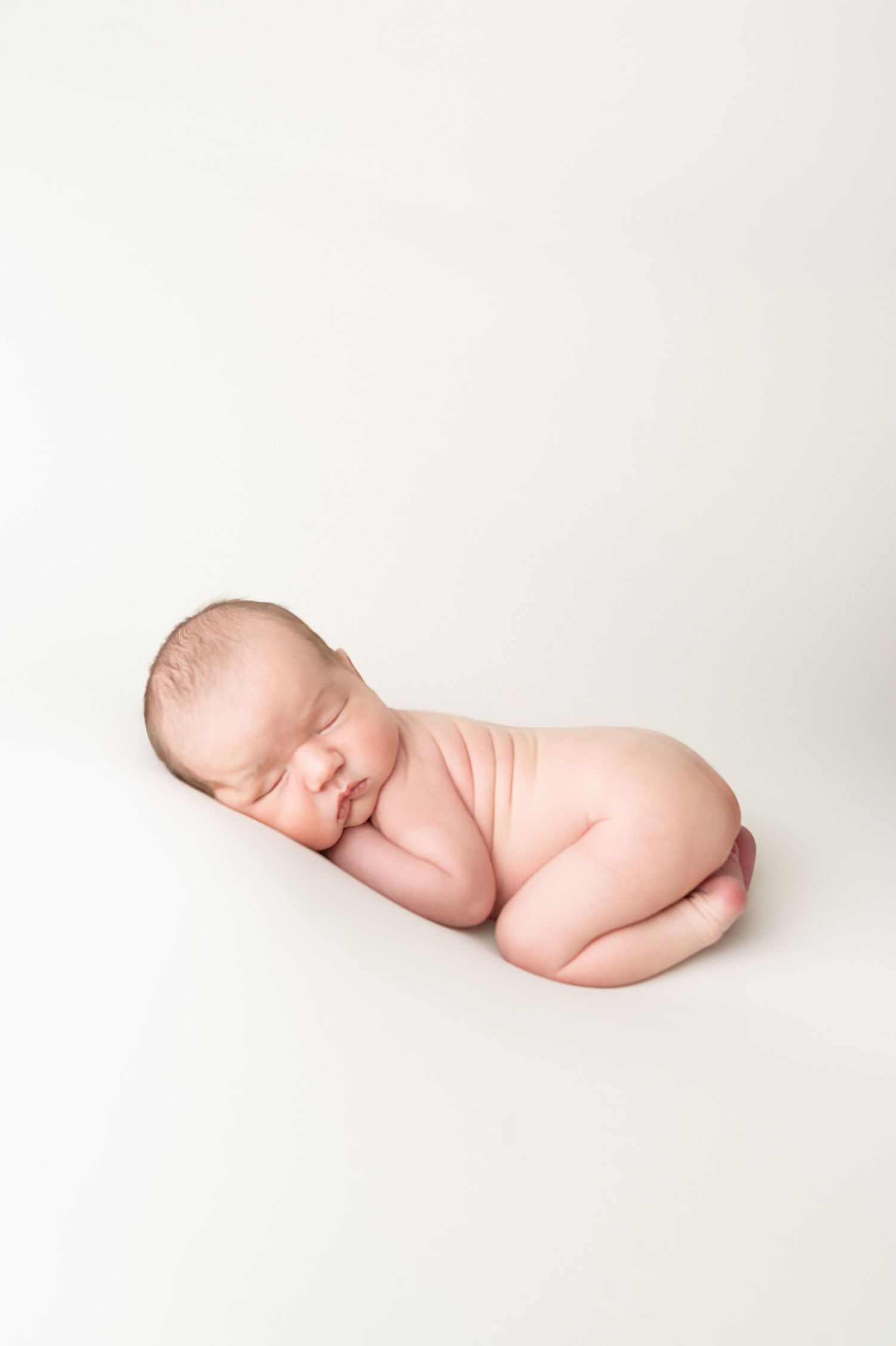 Sleeping newborn baby posed artistically on minimalist white background.