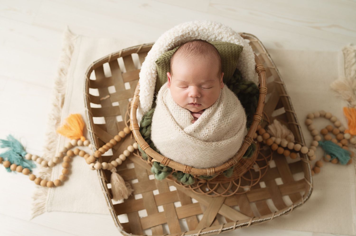 Peaceful sleeping newborn wrapped in white swaddle lying in woven bamboo basket with beaded decorations.