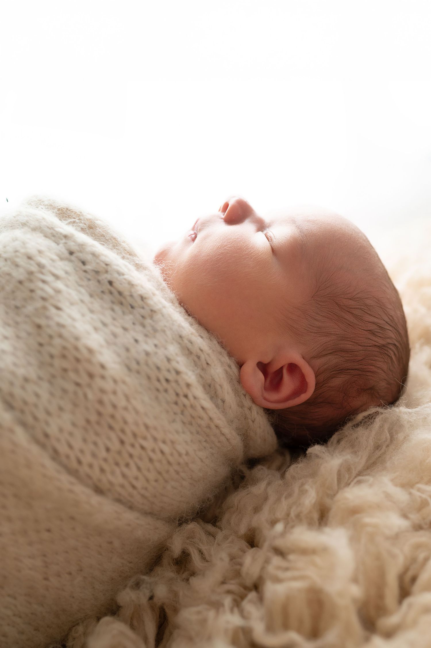 Close-up of sleeping newborn in knit wrap against textured cream background.