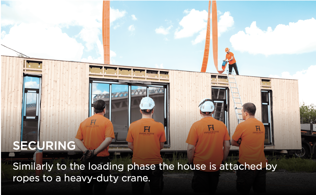 Construction crew lifts modular house section using crane beams and forklifts during prefab home assembly process.