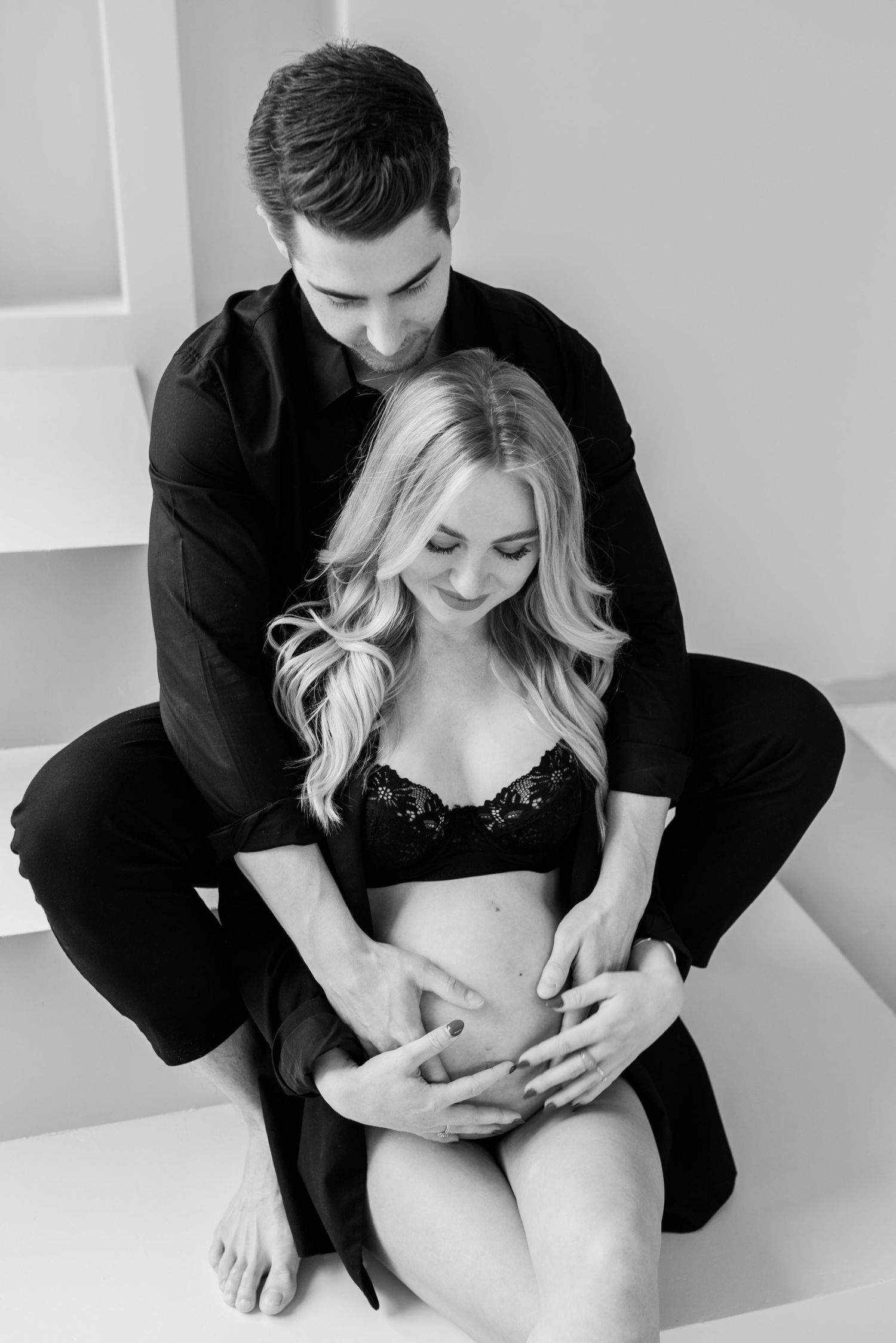 A romantic black and white intimate photo of a couple embracing in minimal studio setting.
