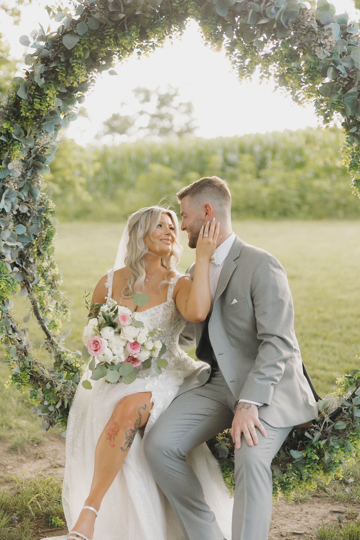 A couple shares intimate moments under a floral arch in an outdoor photoshoot with a gray and white color scheme.