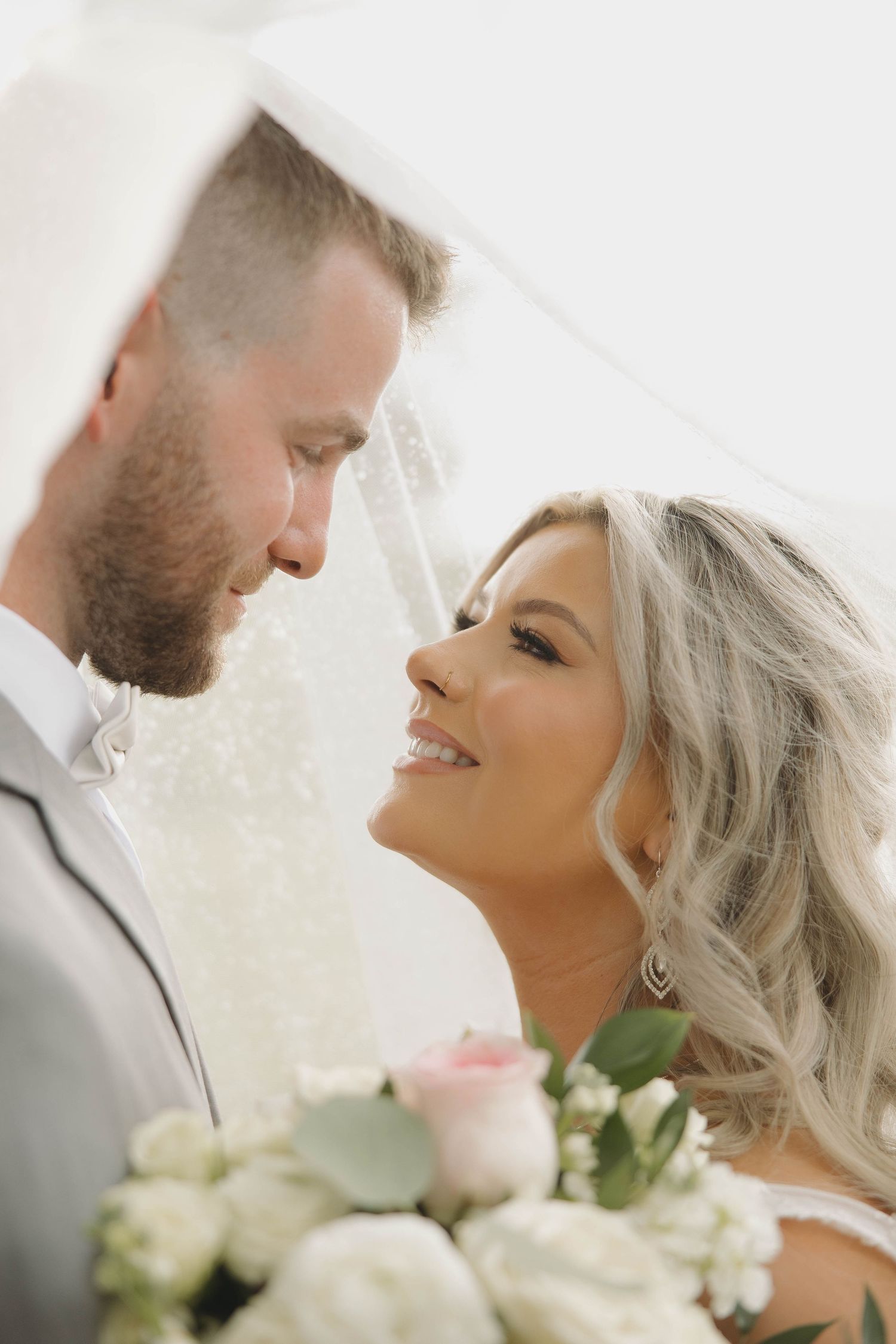 A romantic close-up portrait of a couple on their wedding day with white roses and elegant lighting.