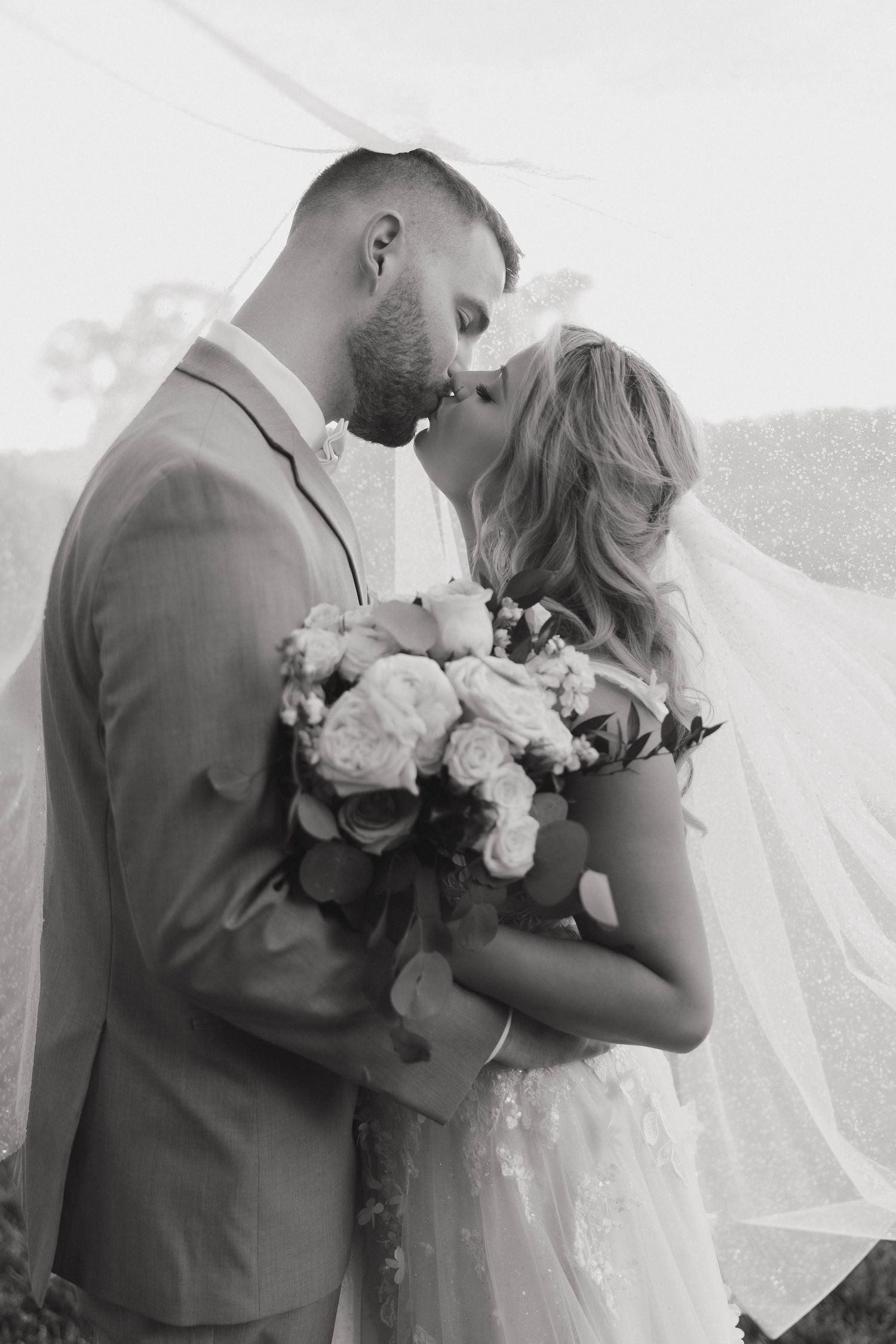 A romantic black and white photo series shows a couple sharing tender moments with a wedding bouquet of white flowers.