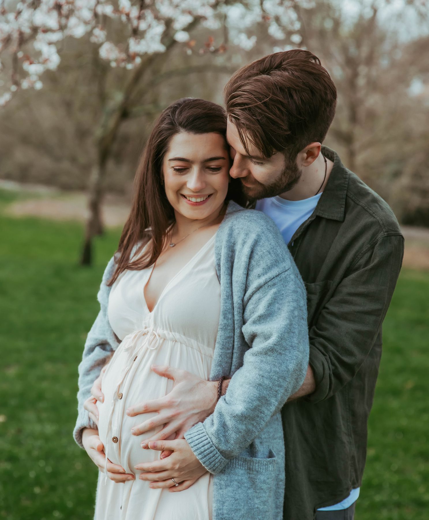Romantic couple shares intimate moments in an orchard setting while embracing an expectant mother's baby bump. At a maternity photoshoot
