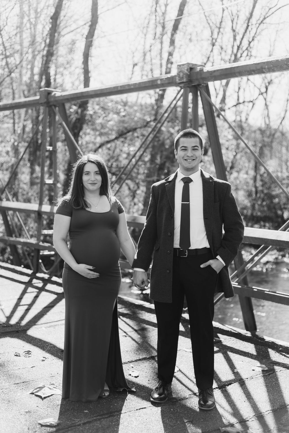 A black and white photoshoot of a couple on a bridge with dramatic shadows and industrial elements.