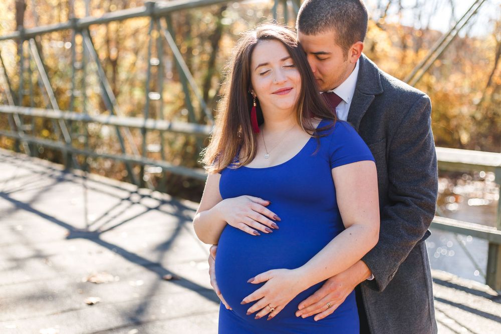 A couple embraces while standing against a bright outdoor backdrop.