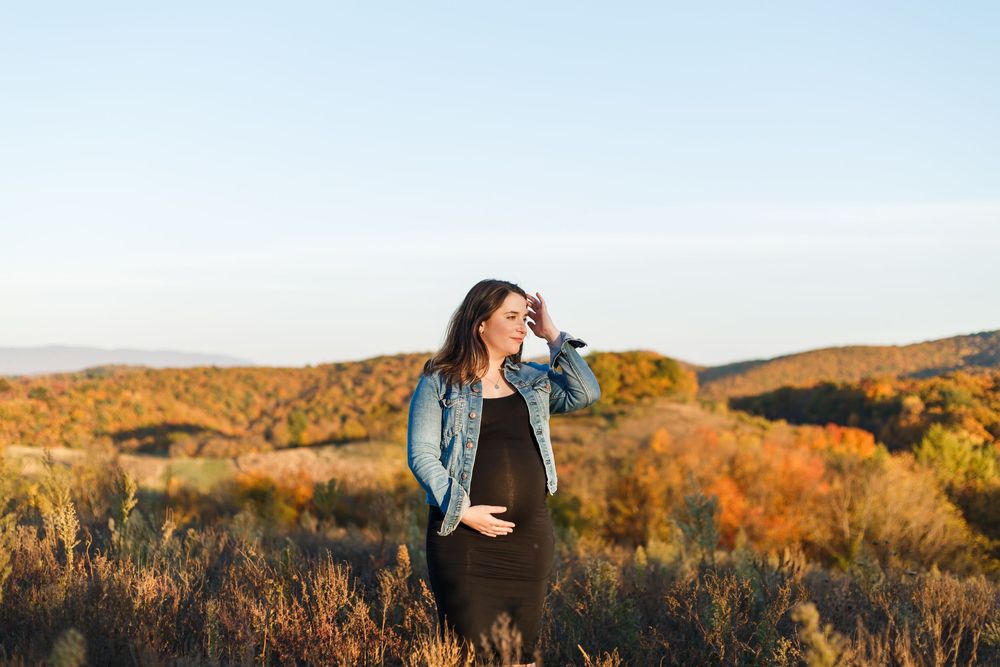 Woman in black dress twirls against backdrop of autumn mountains with golden foliage at sunset.