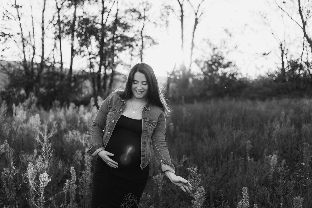 Black and white portrait of pregnant woman laughing while standing in a wild meadow.