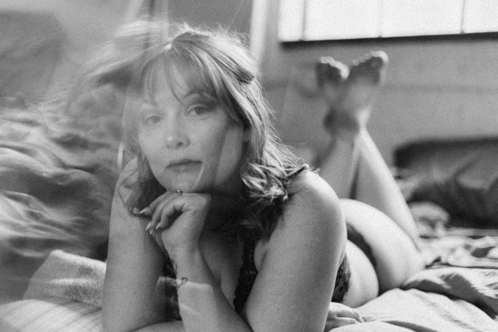 A black and white boudoir photograph of someone posing on a bed in vintage style.