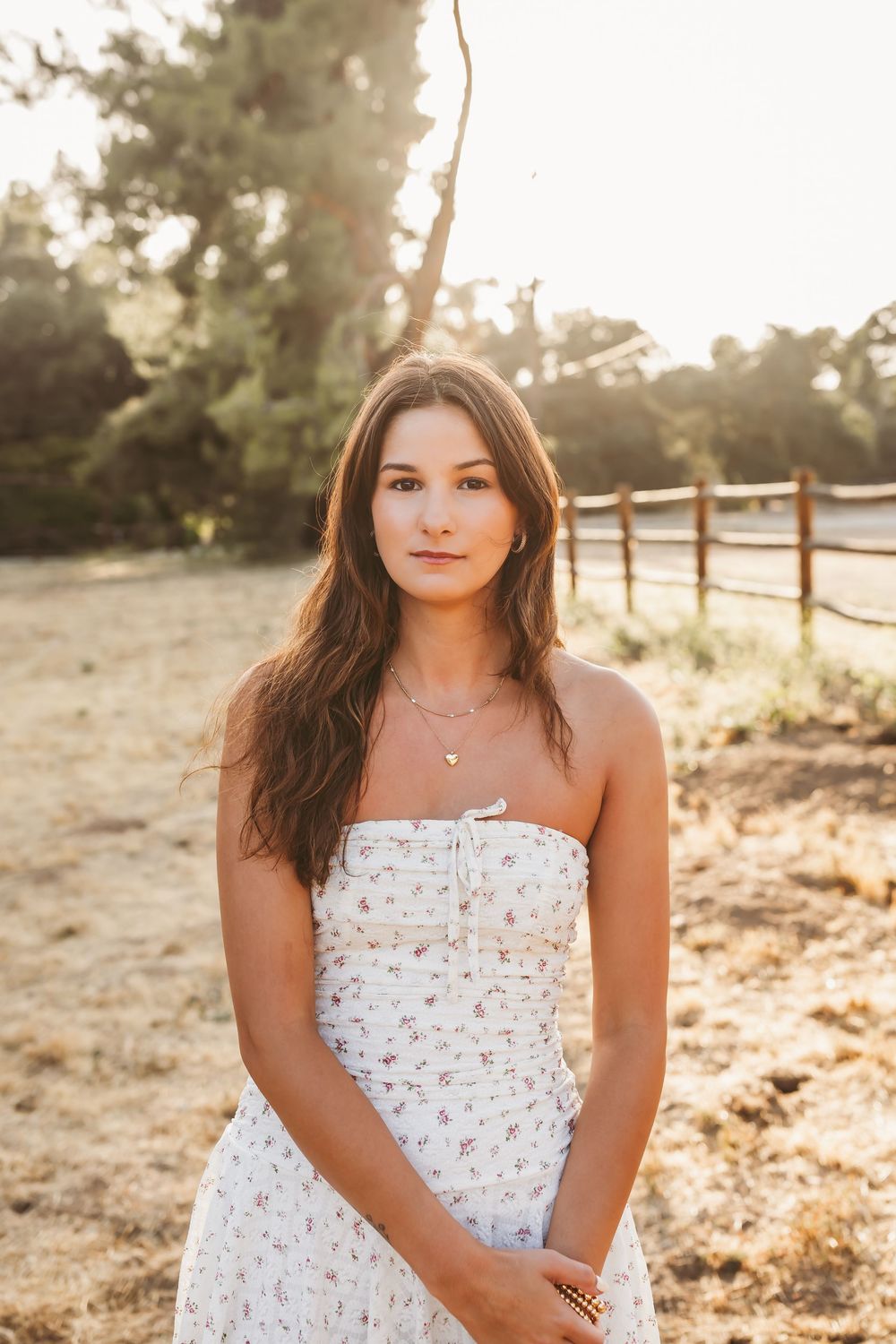 A collection of golden hour outdoor portraits showing someone wearing a white floral sundress in a rustic field setting.