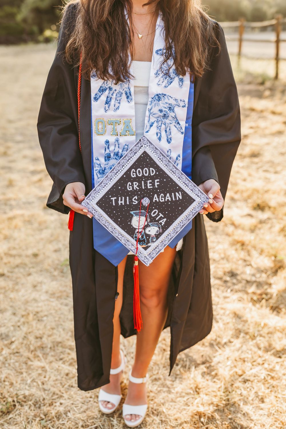 Graduation cap decorated with black and white Snoopy design reading 'Good Grief. This Again' with blue floral stole.