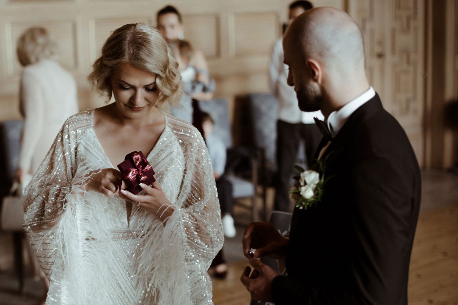 Two people share an intimate moment during a wedding ceremony, with the bride wearing a lace white dress and holding flowers.