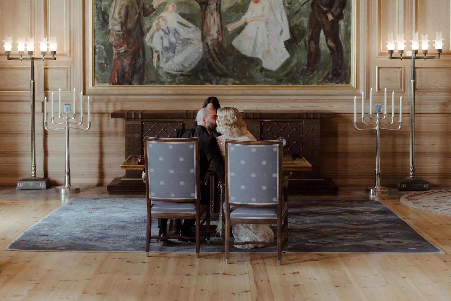 An elegant grand hall with ornate wall paintings, antique chairs and chandeliers in a luxurious historic palace setting.