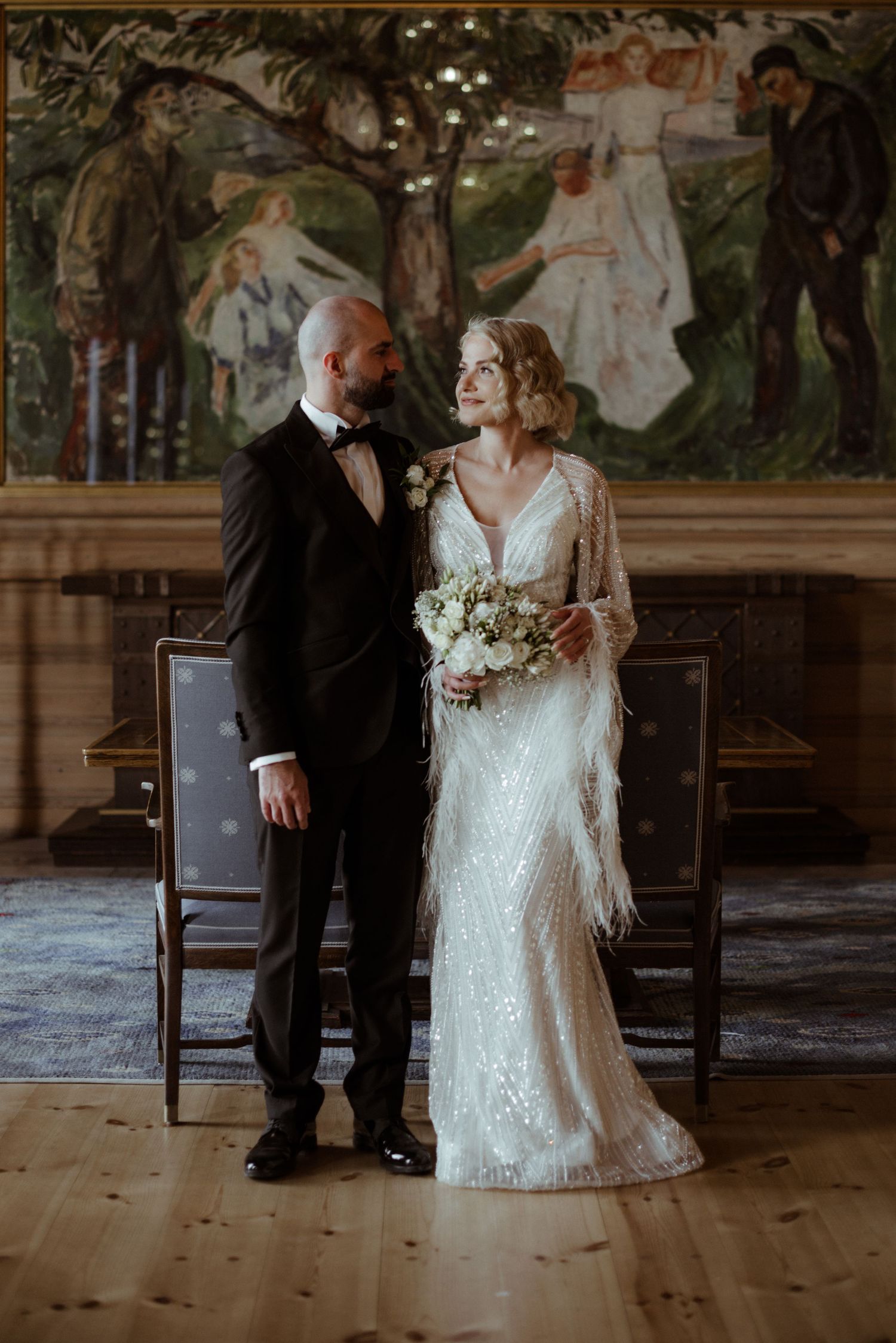 Newlywed couple stands together in rustic venue with wooden floors and elegant vintage decor for wedding photo.