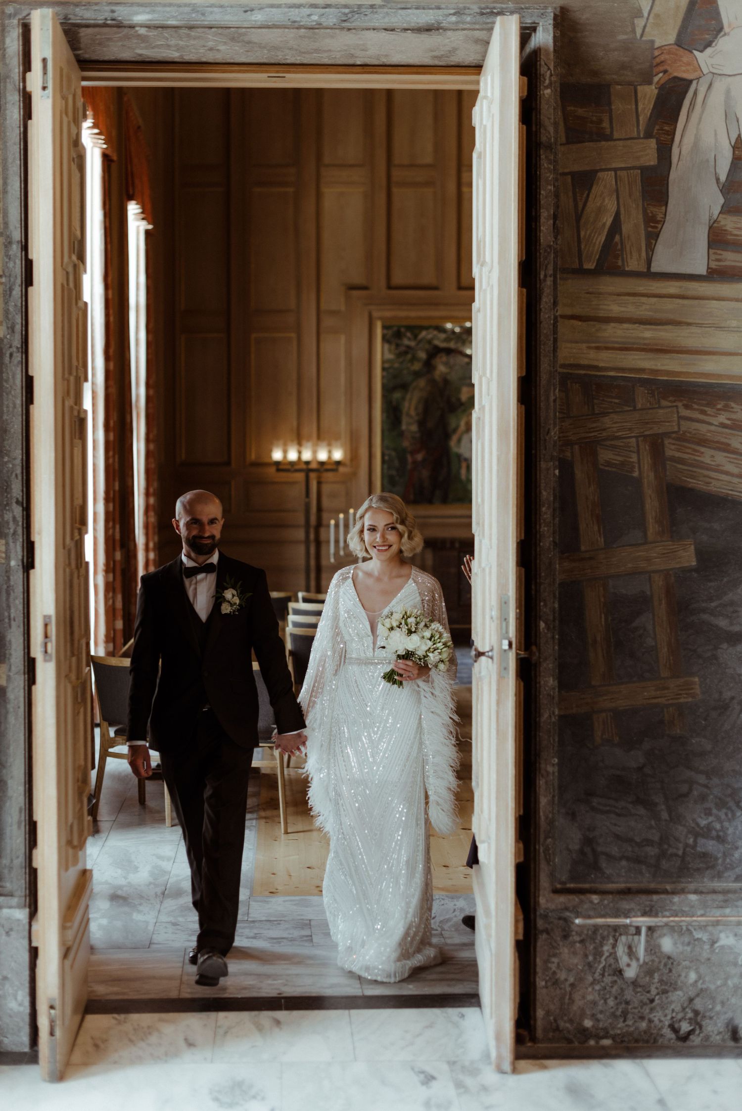 A couple walks hand in hand through a rustic wooden doorway in their formal wedding attire.