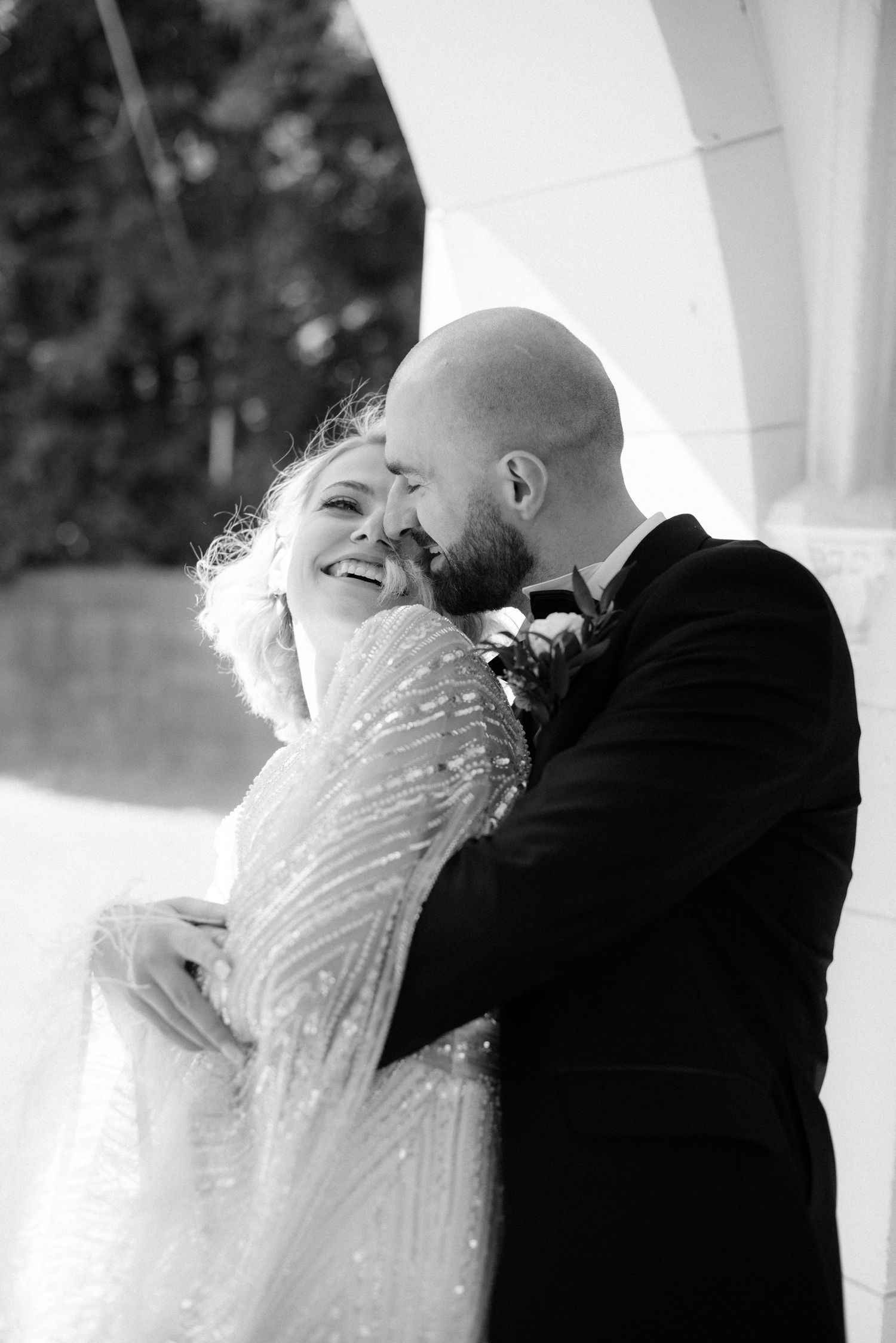 A romantic black and white wedding photo of a couple embracing and laughing together in formal attire.