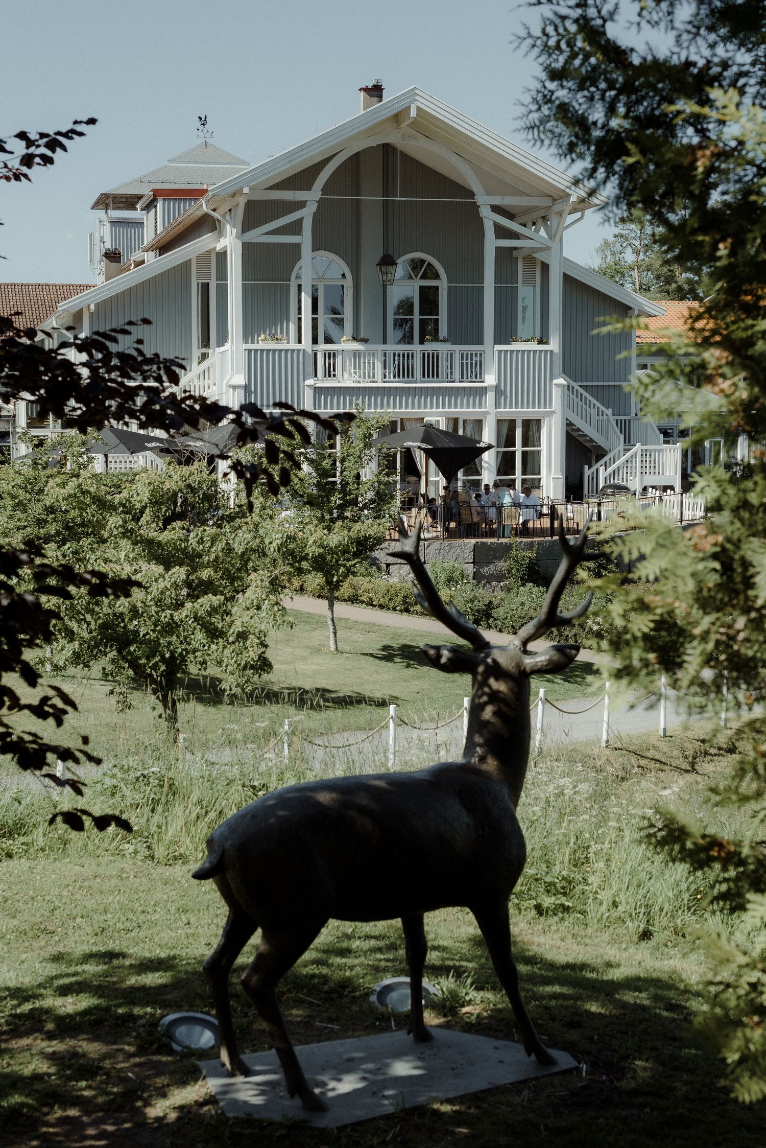 A decorative deer statue stands in a garden with a white Nordic-style house featuring a covered porch in the background.
