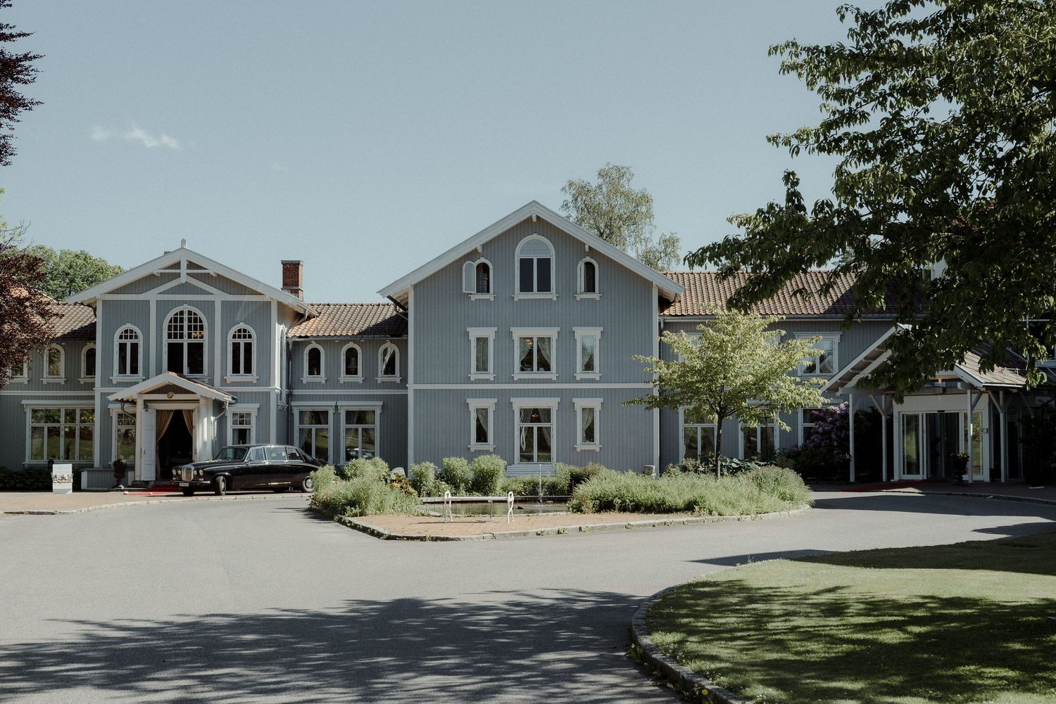 A charming historic blue-gray building complex with white trim and a circular driveway surrounded by landscaping.