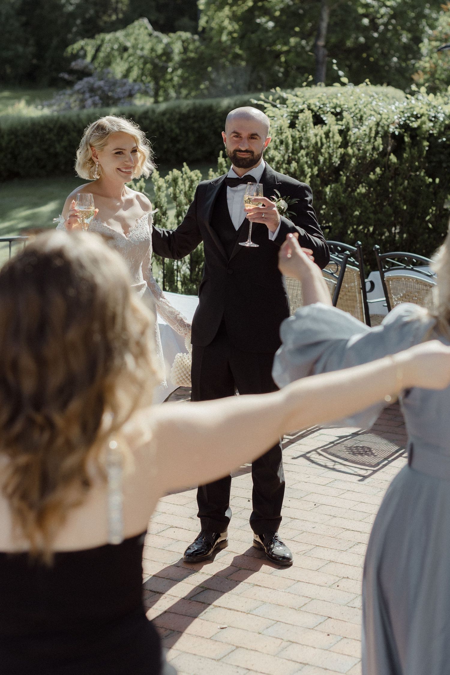 A joyful celebration at an outdoor garden wedding ceremony on a paved stone patio in summer sunshine.