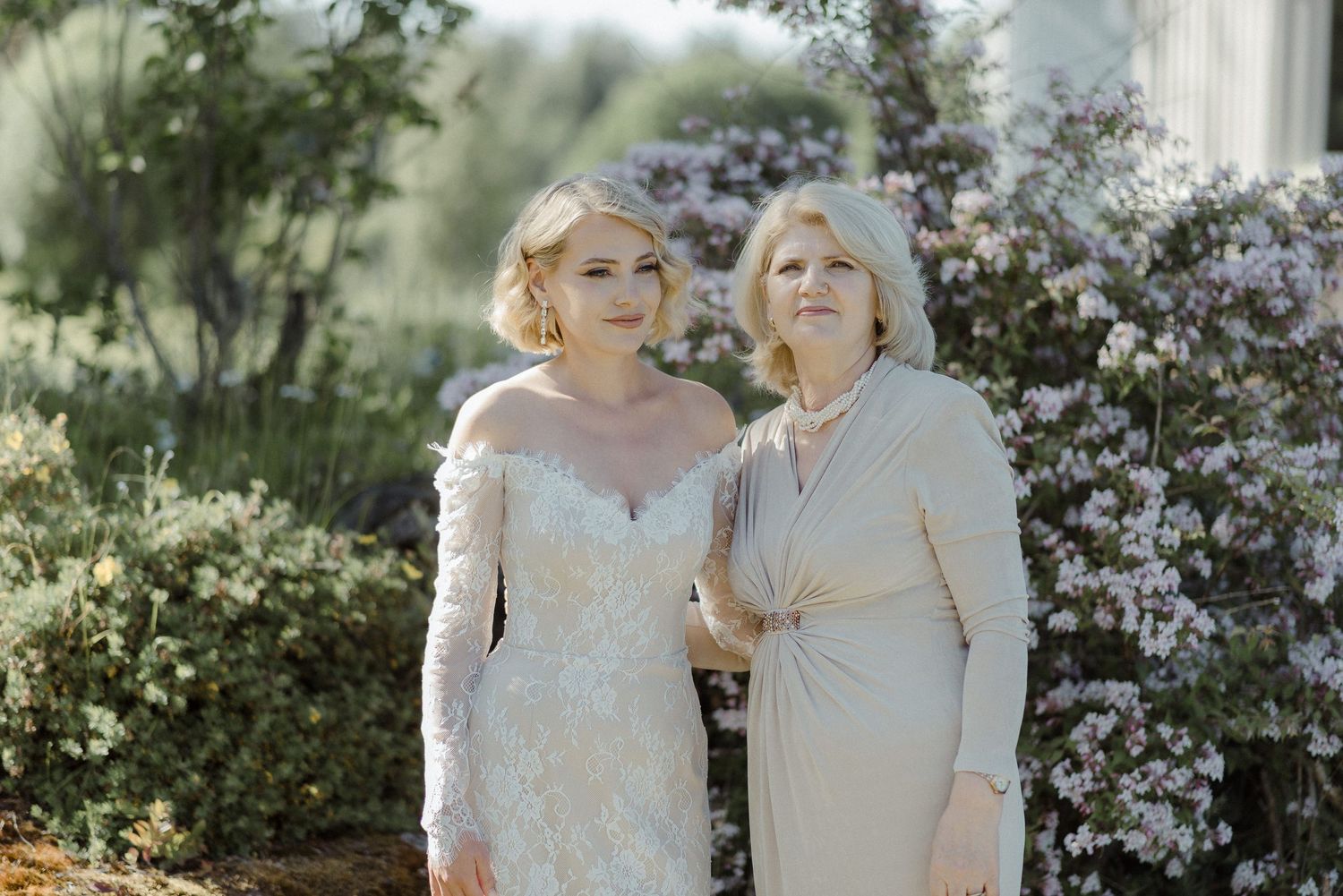 Two people pose together in a garden setting with white flowers in the background.