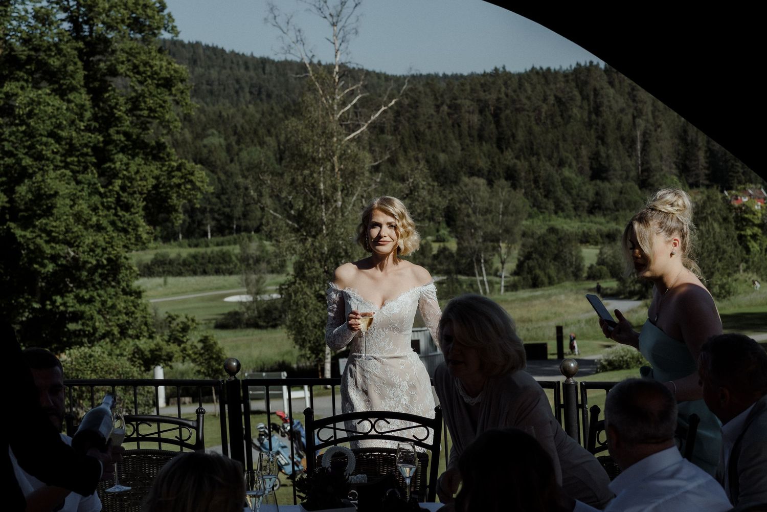 Outdoor wedding reception setup in a scenic mountain landscape with guests gathered at long tables in nature.