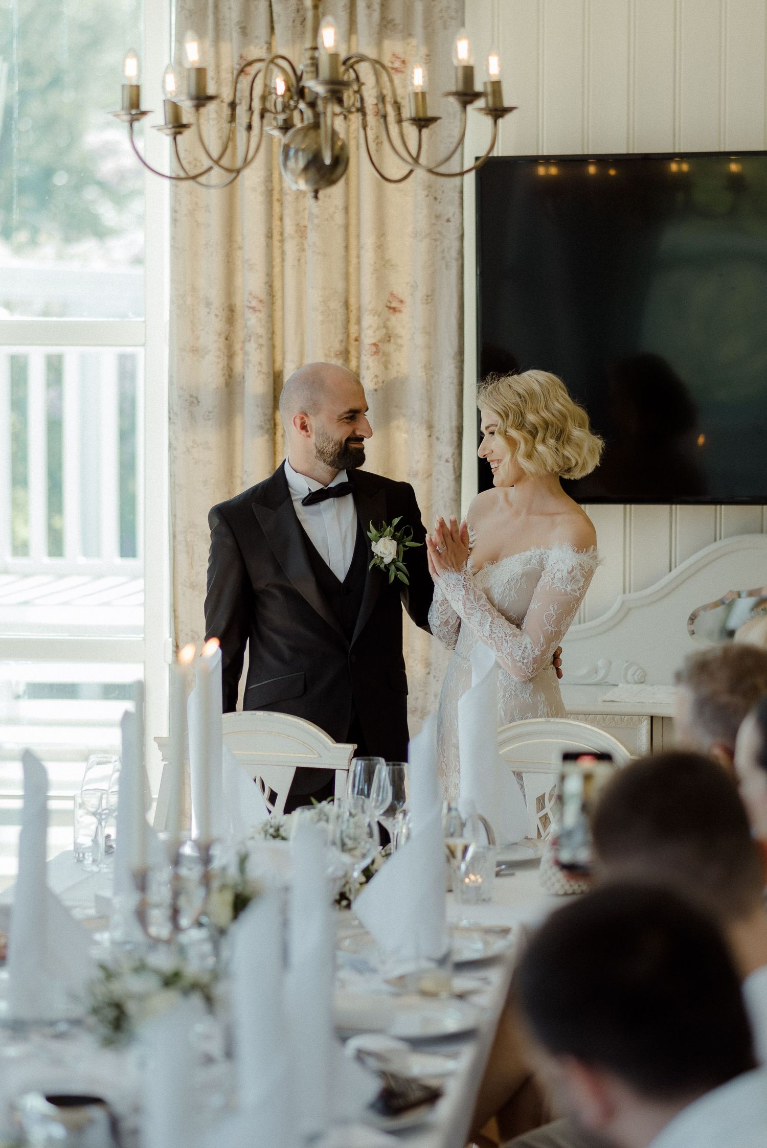 An elegant wedding reception set in a bright room with a brass chandelier and white table settings.
