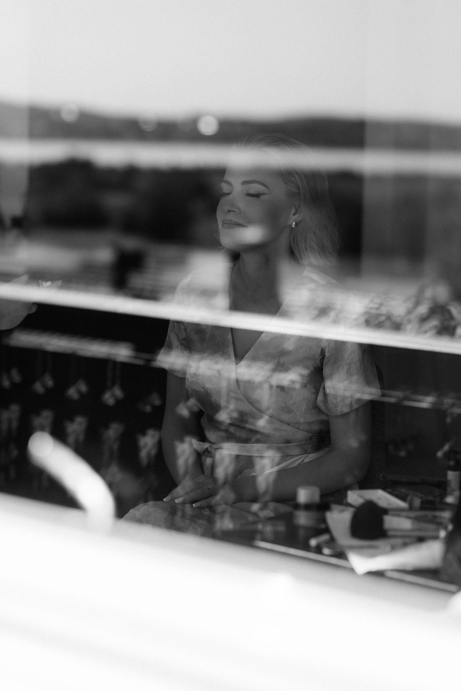Black and white artistic photograph showing a reflection in a window with soft bokeh lights in the background.
