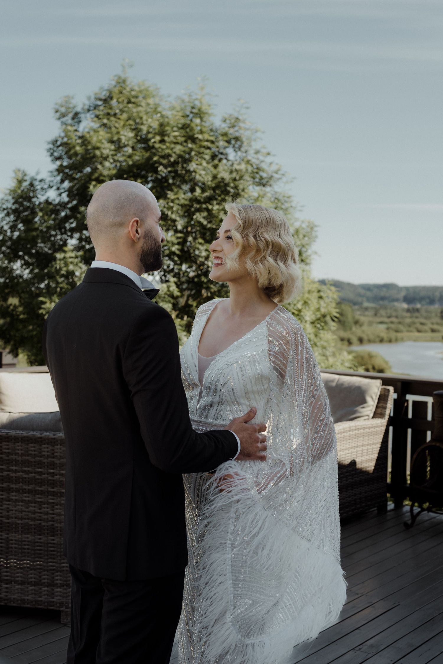 Two people in wedding attire share a romantic moment on a scenic deck overlooking water and mountains on their special day.