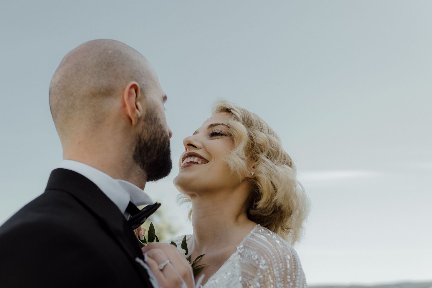 A couple laughs and embraces during a romantic wedding photoshoot against a white sky background.