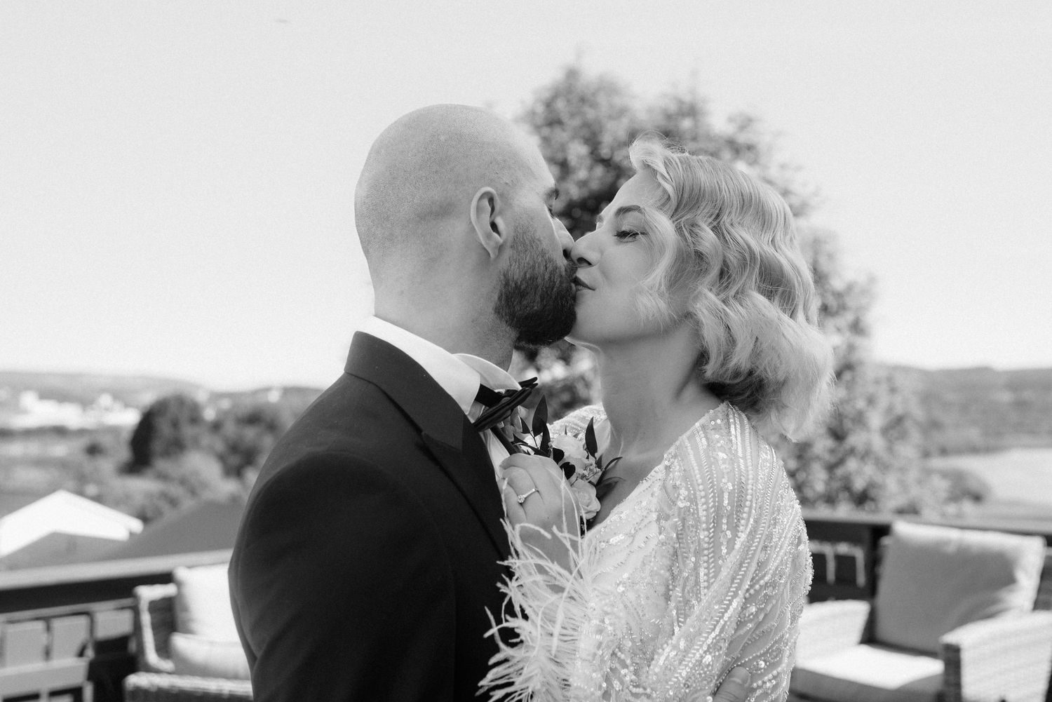 A couple shares a romantic kiss on their wedding day, captured in black and white photography with a scenic backdrop.