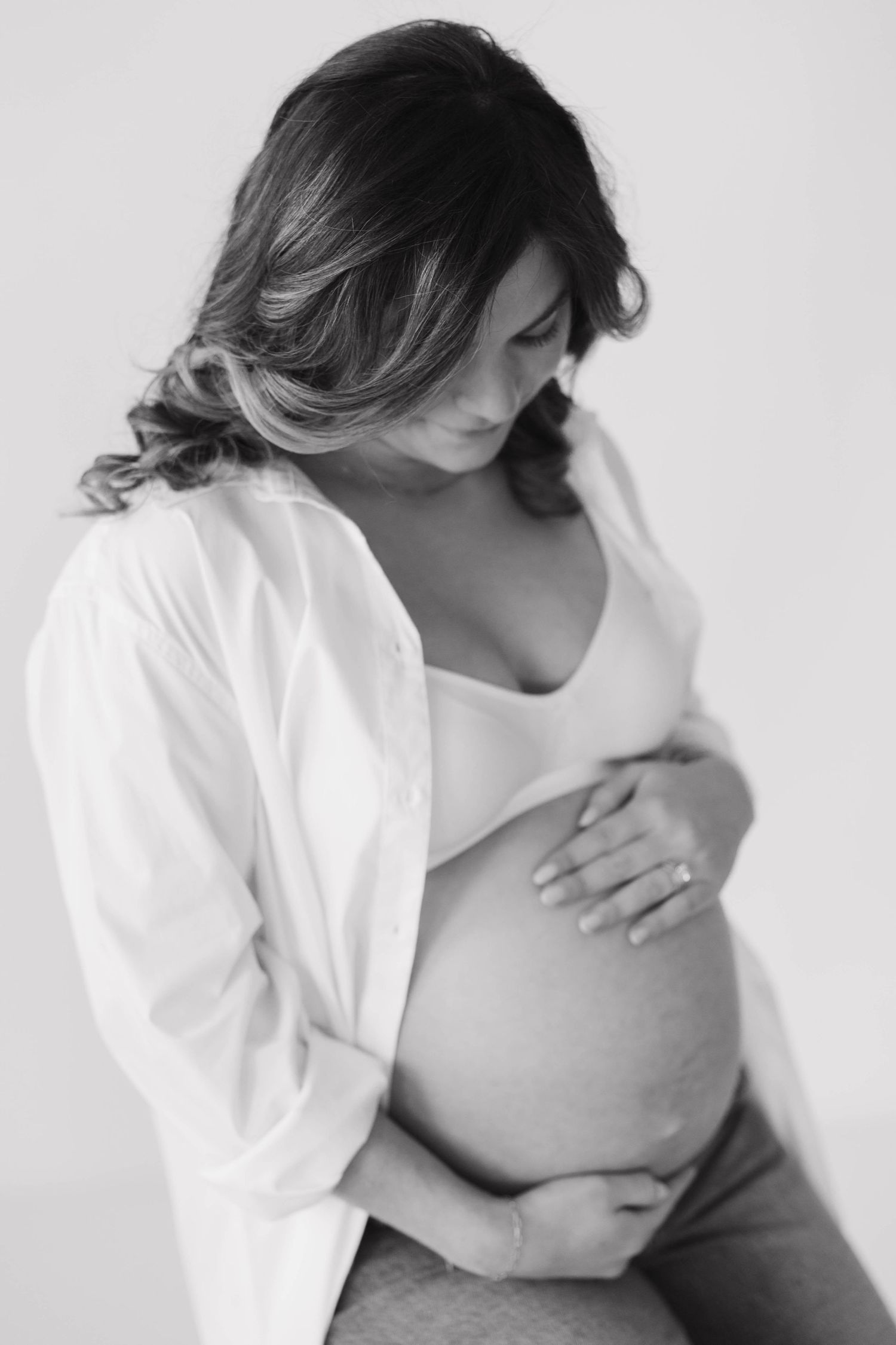 Black and white maternity photo showing a pregnant woman in casual attire holding her belly.