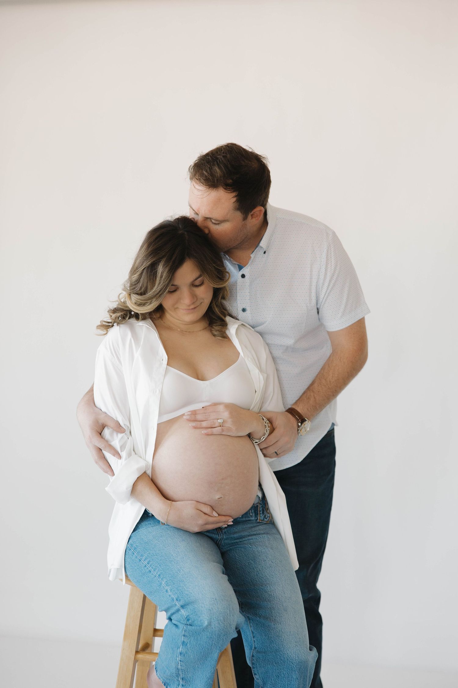 A minimalist maternity photoshoot sequence showing tender moments between an expectant couple against a white backdrop.