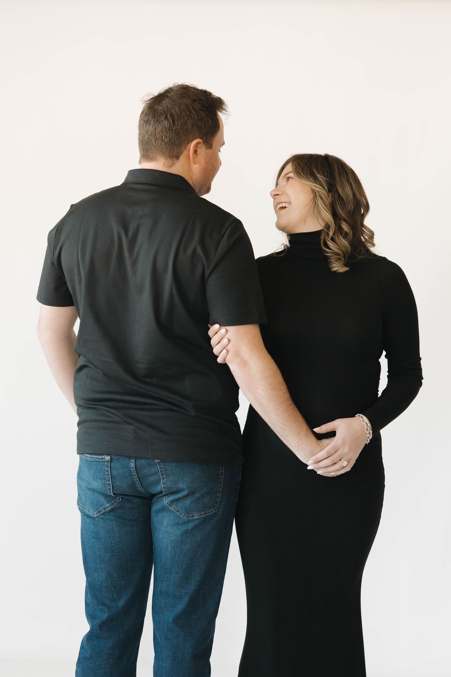 Series of back-facing poses showing a couple in dark clothing embracing against a white wall.