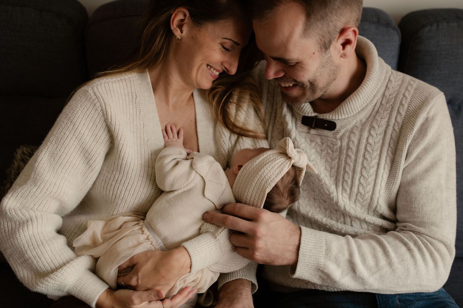 Photo de jeune parents qui regardent leur nouveau né assis dans leur canapé