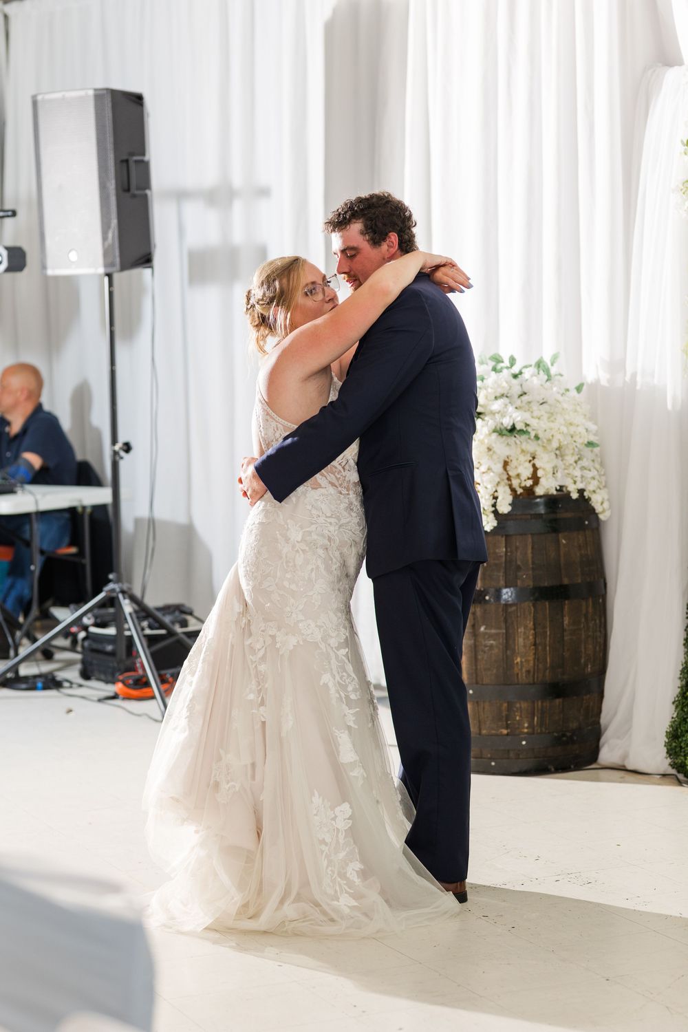 Couple shares their first dance at a rustic wedding reception with wooden barrel decor and white draping.