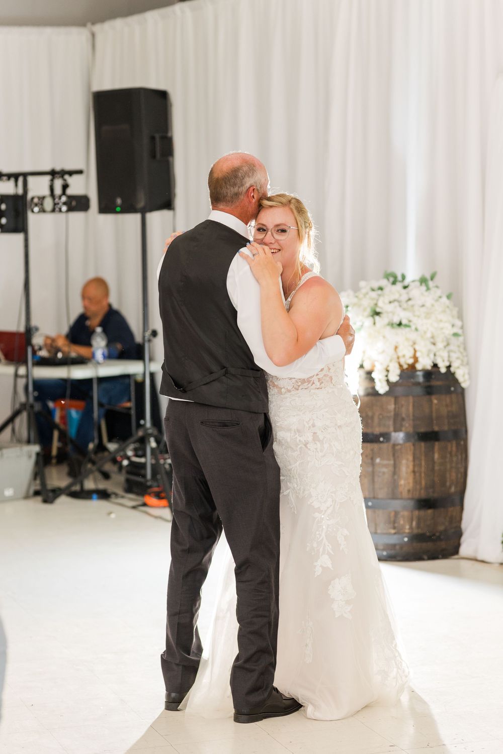 A romantic first dance between newlyweds at an elegant white reception venue with rustic wine barrels decorating the space.