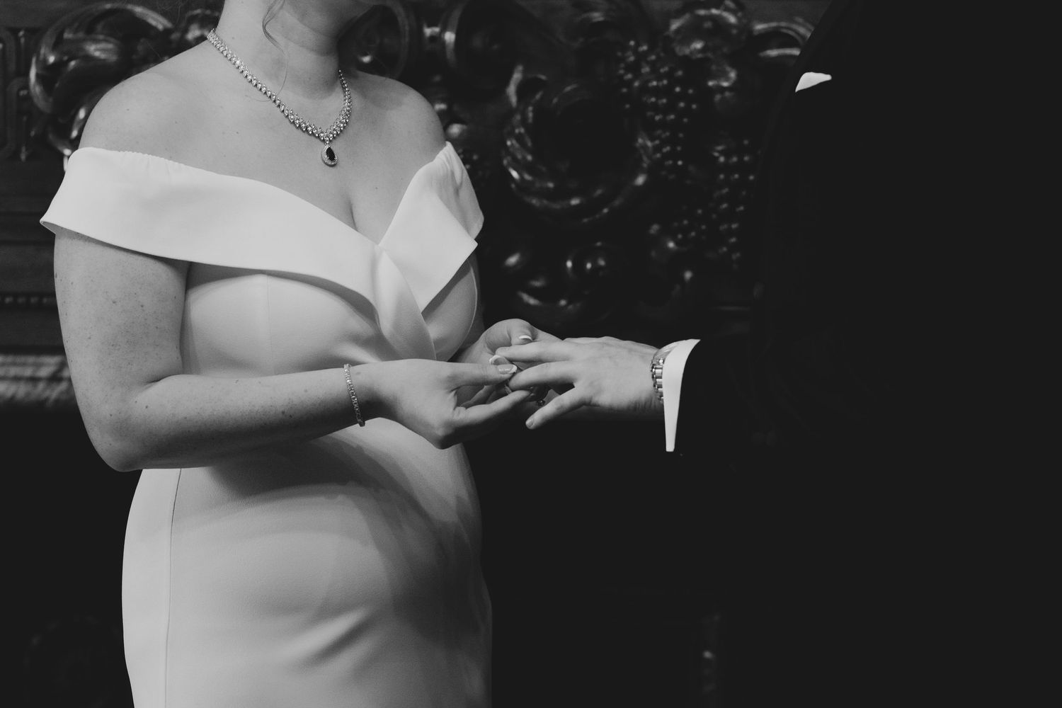 Black and white close-up photo of a couple exchanging rings during a wedding ceremony.